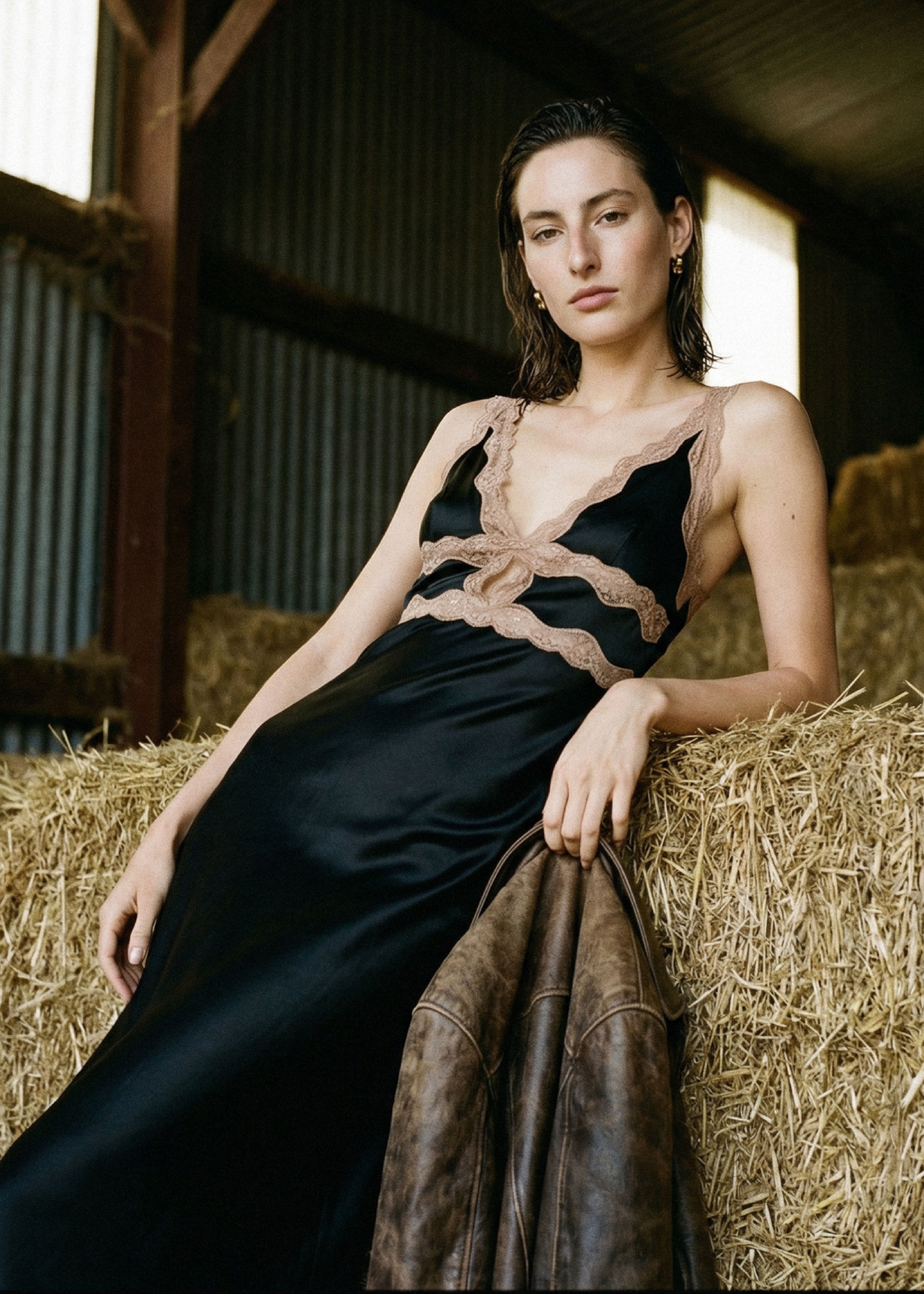 Woman in a black dress posing against hay bales in a barn.