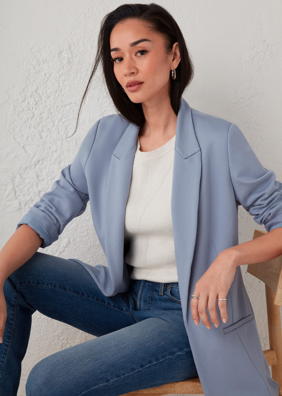 A woman in a blue blazer and jeans, sitting confidently.