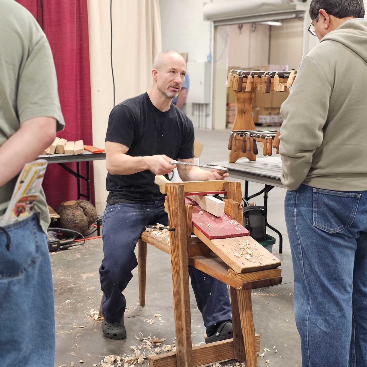 A man demonstrates woodworking techniques to an audience at an event.