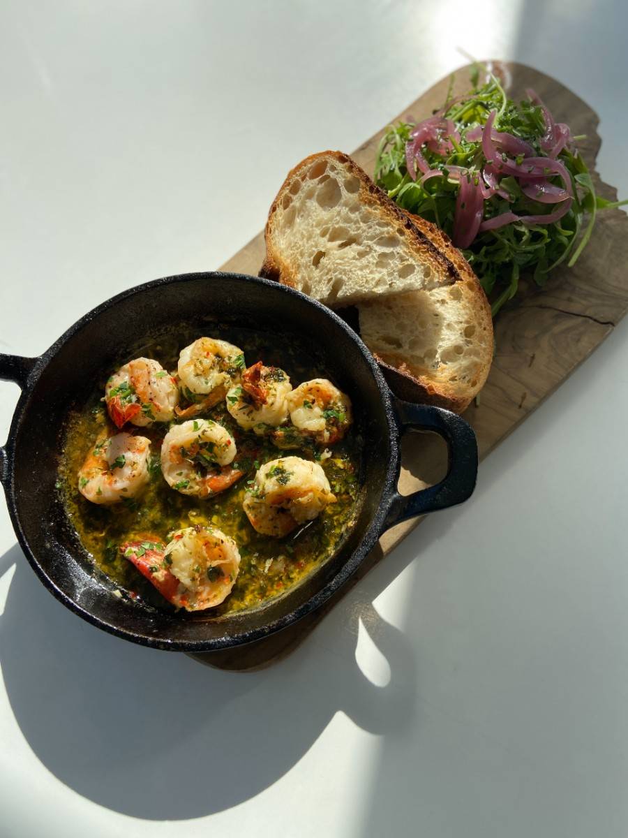 A skillet of grilled prawns with bread and salad on a table in the sunshine at The Factory Kitchen cafe in Newcastle