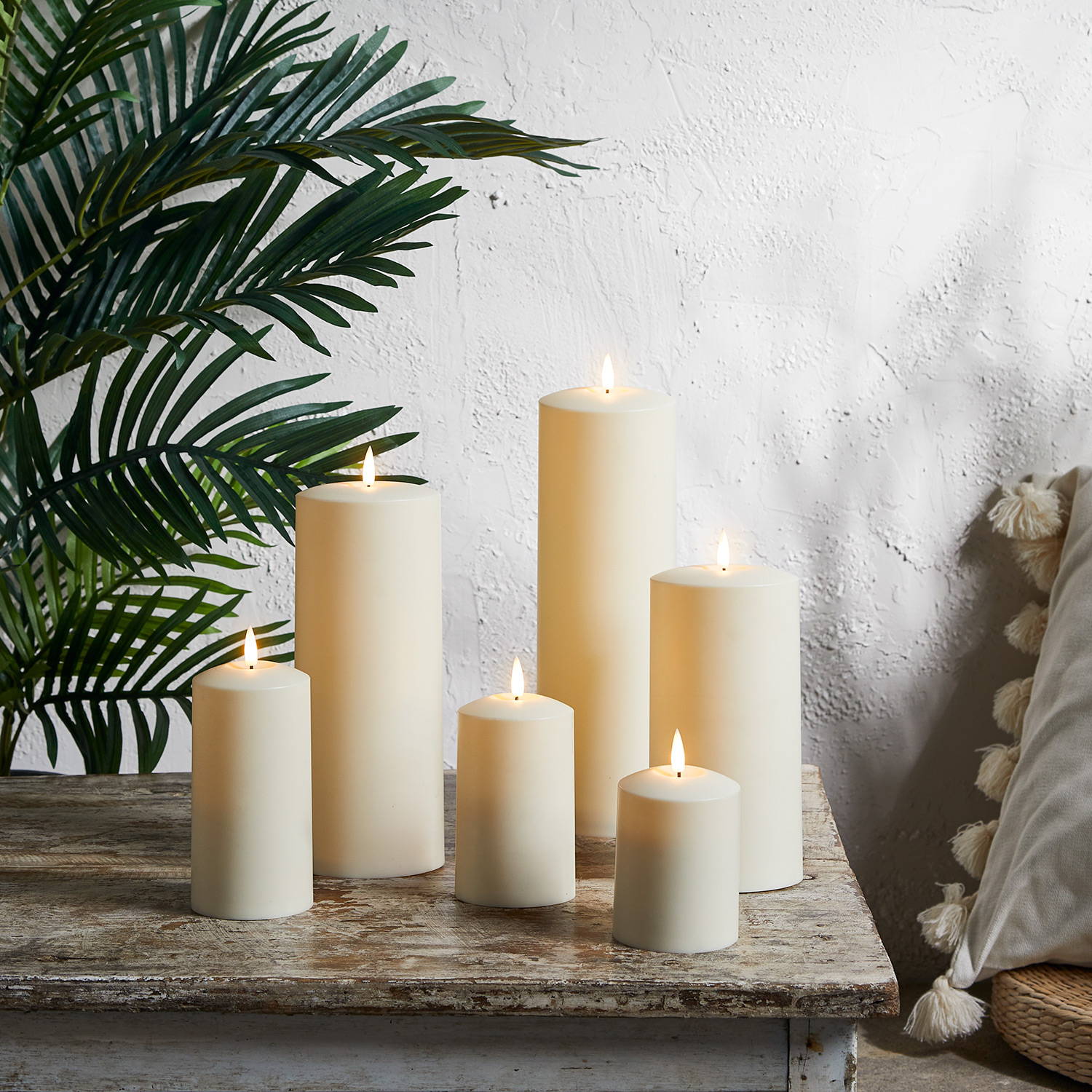 A collection of realistic TruGlow battery candlescandles sat on a table with some green foliage behind