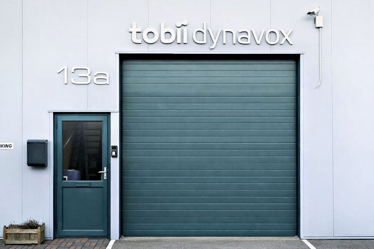 Grå garasjeport med en liten sidedør og et skilt med “Tobii Dynavox”.