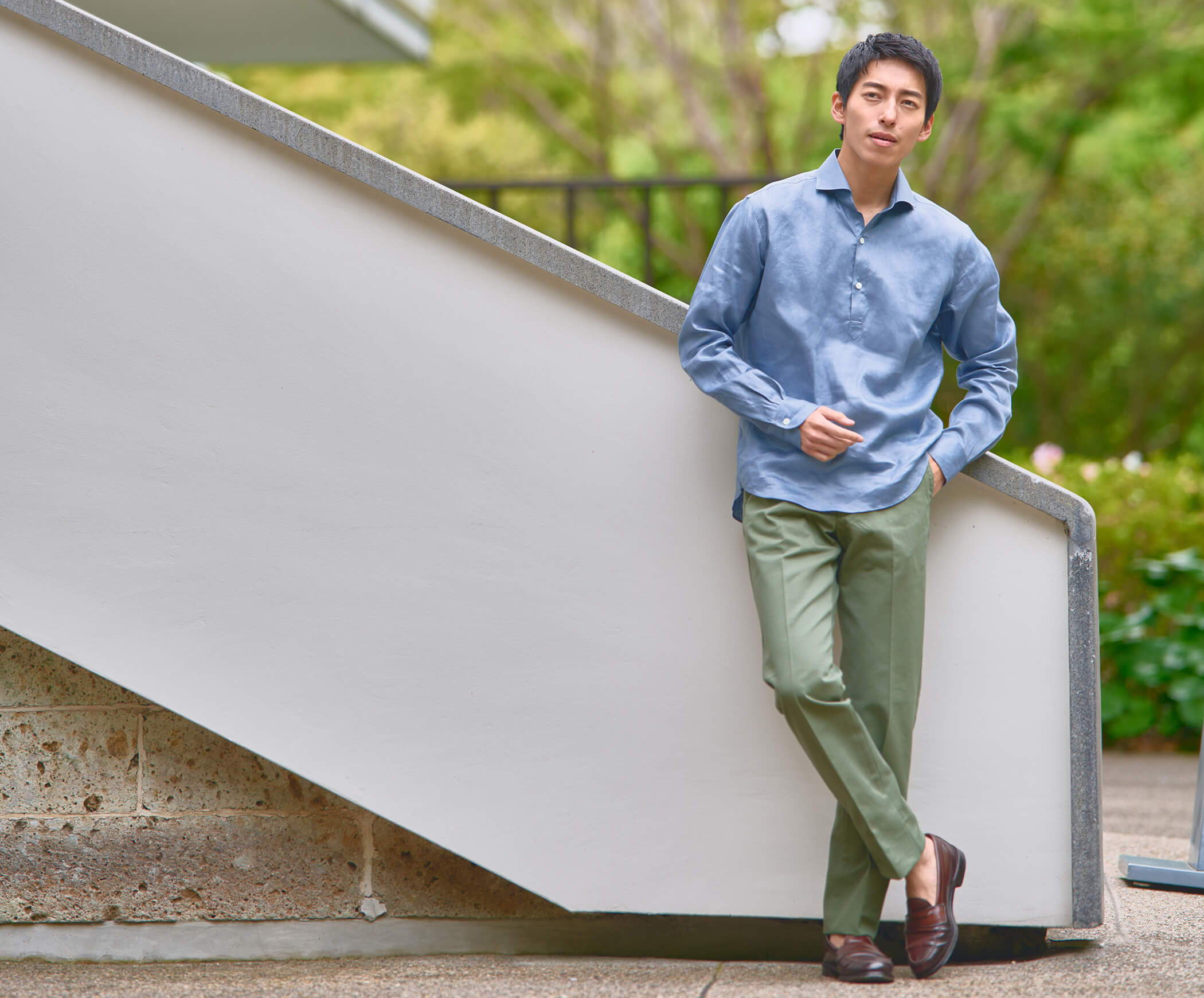 A person in casual attire leaning against a wall outdoors.