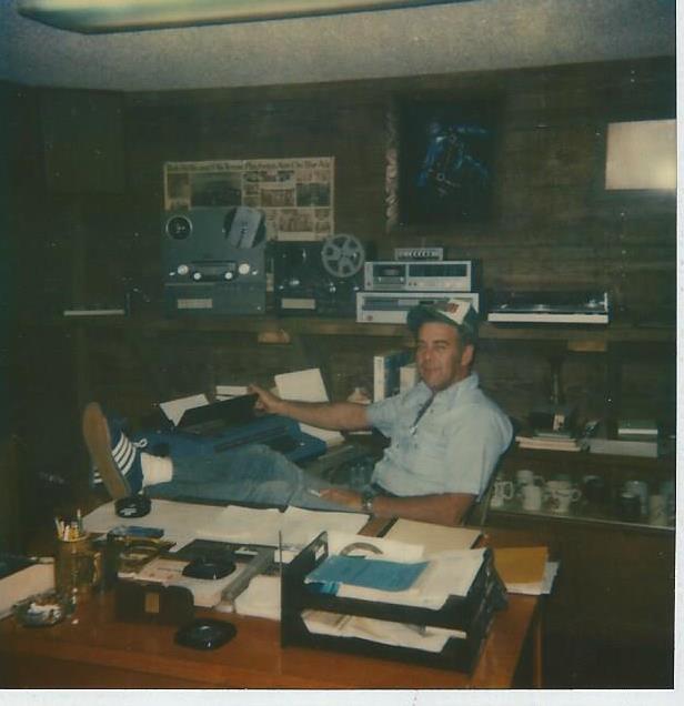 Mr. Walton sitting at a desk with equipment and papers in a dimly lit office.