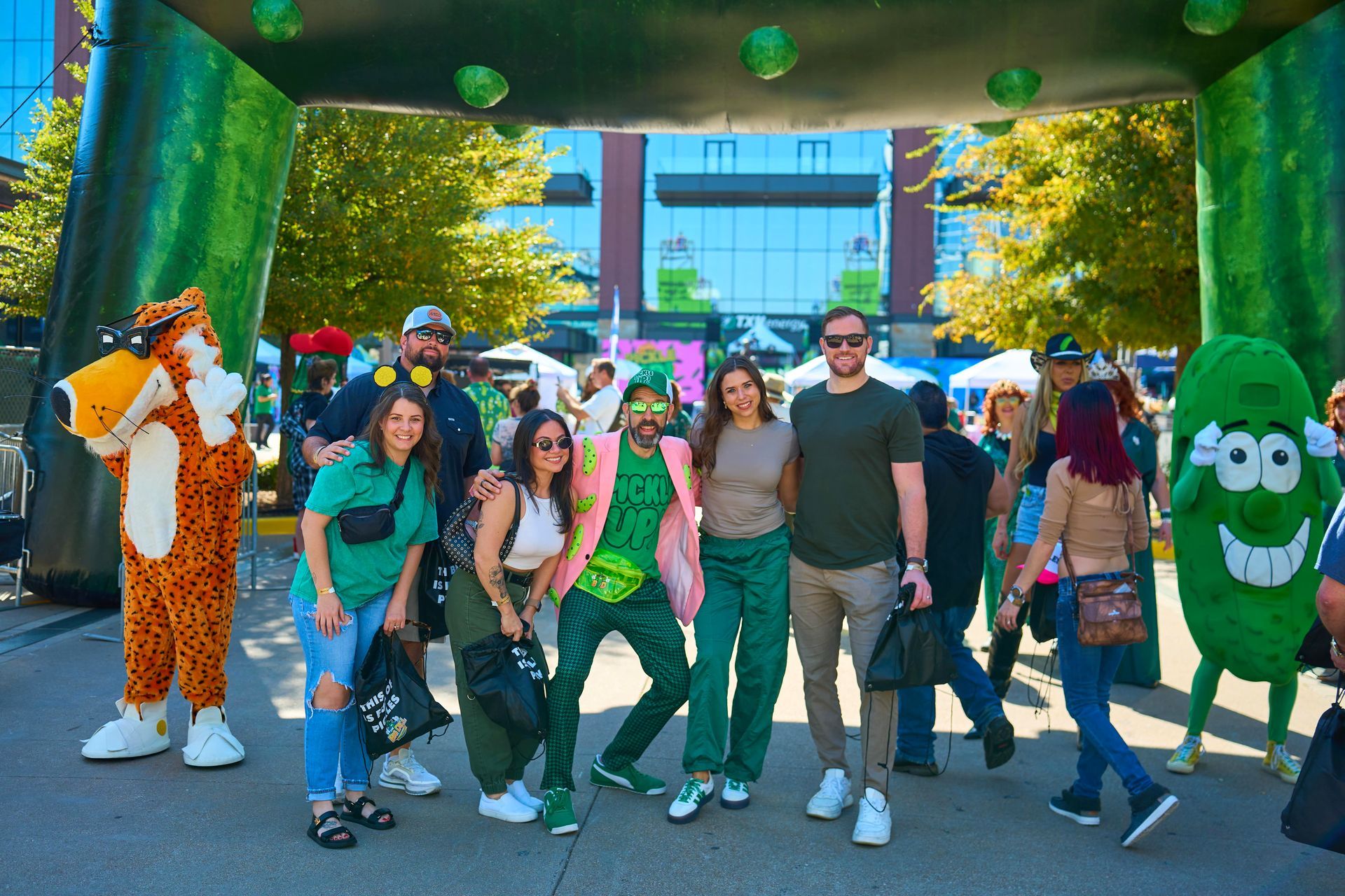 A group of festival guests pose with the Cheetos mascot under The Big Dill 30-foot inflatable pickle arch at The Big Dill pickle festival, Globe Life Field and Texas Live!, Arlington Texas 2025