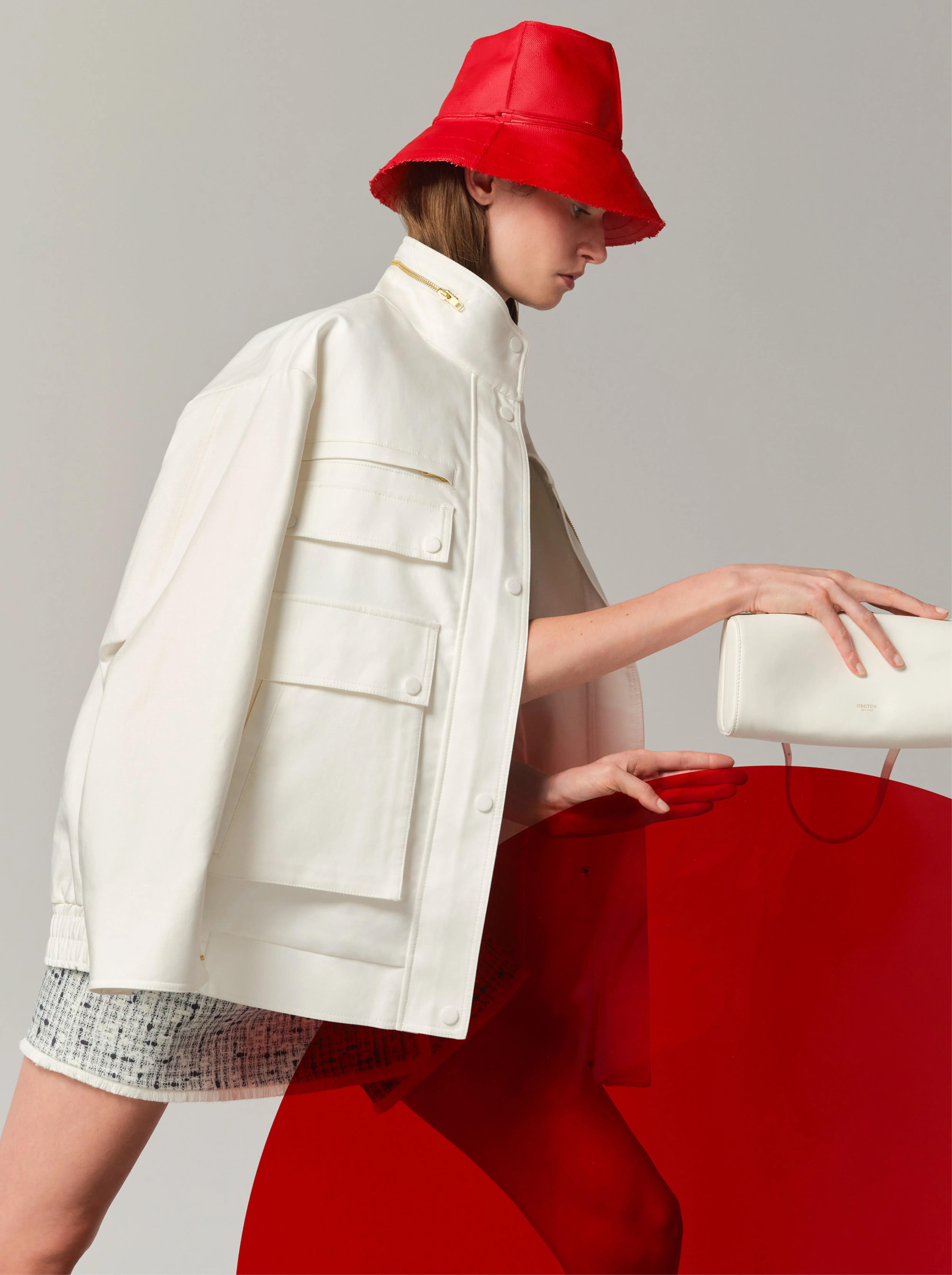 Model wearing a white jacket and red bucket hat, posed with a red background.