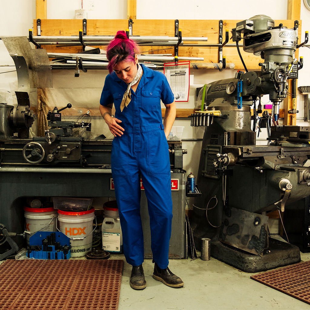 Person in blue jumpsuit standing in a workshop with machinery.