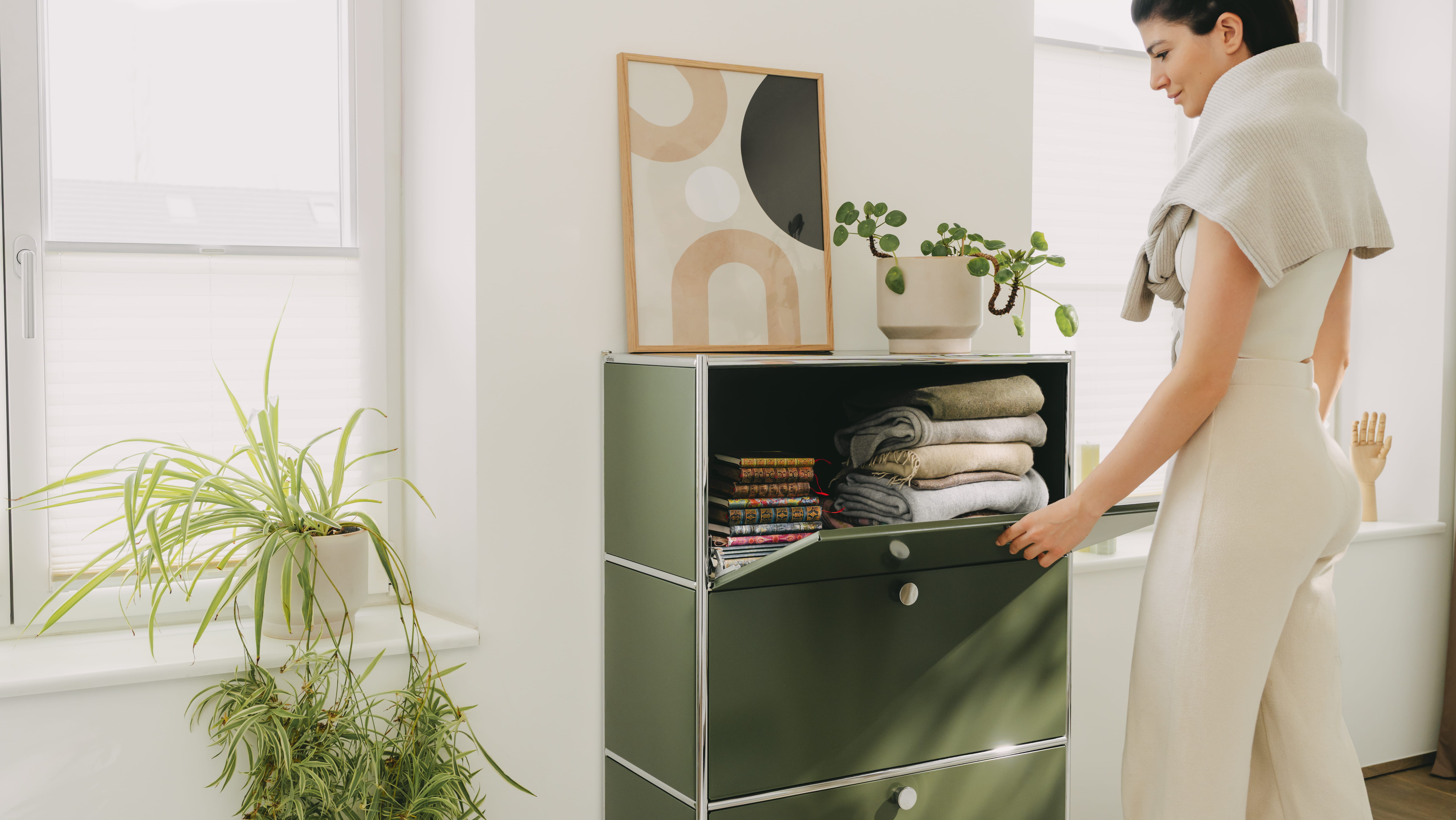 A woman is using the olive-green " Cubox " office shelf from ofinto in her home office