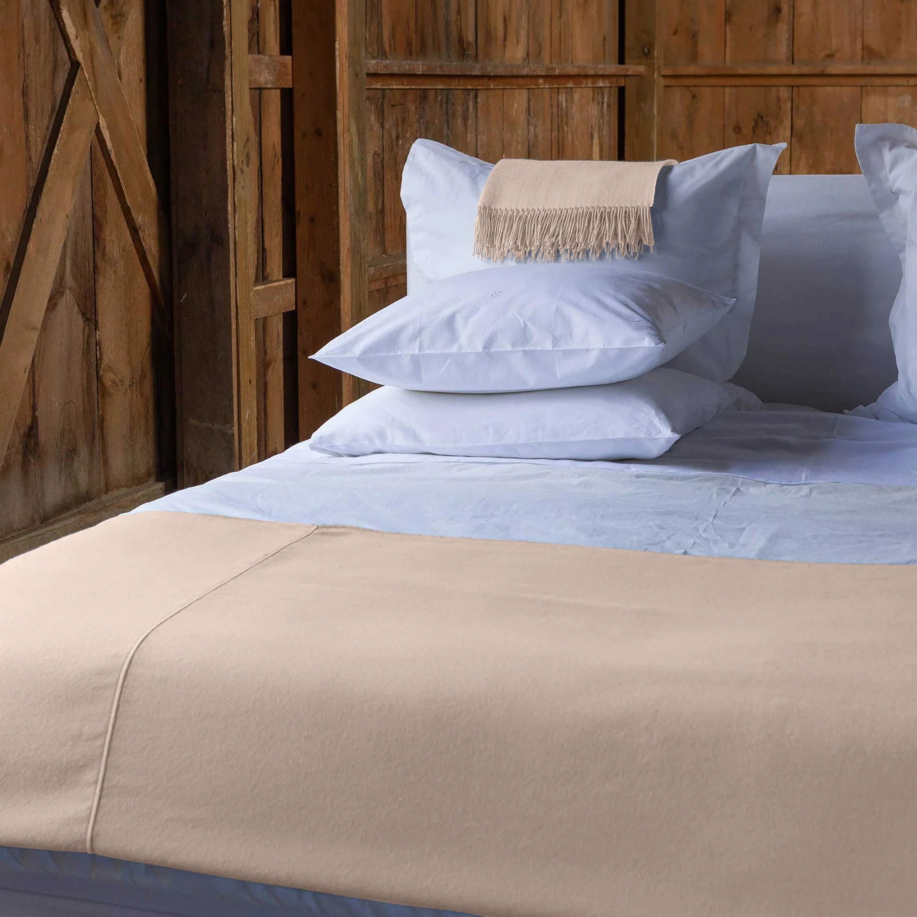 Bedding with pillows on a wooden bed in a rustic setting.