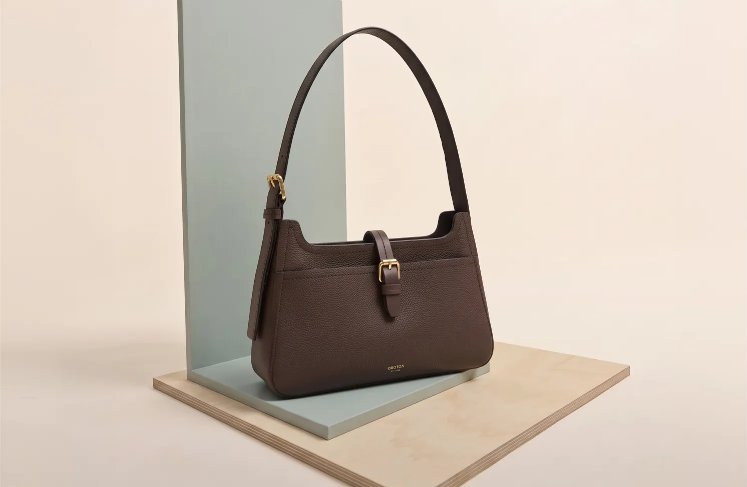 A brown handbag displayed on a minimalist pedestal.