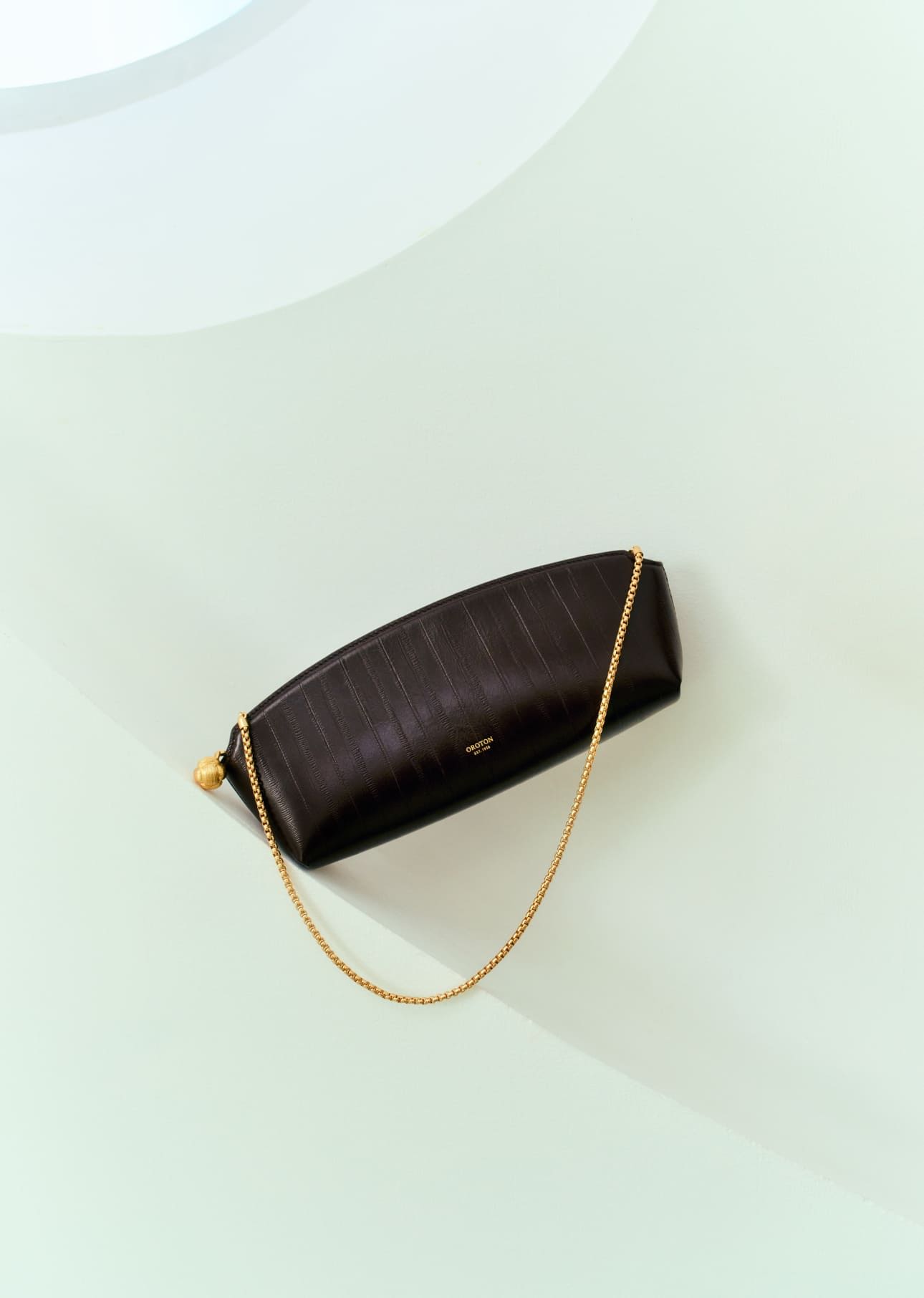 A brown handbag with a gold chain on a light background.