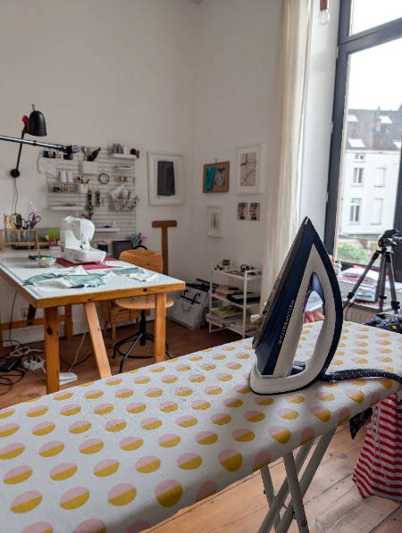 a sewing room with an ironing board and iron and a desk in the background with a sewing machine