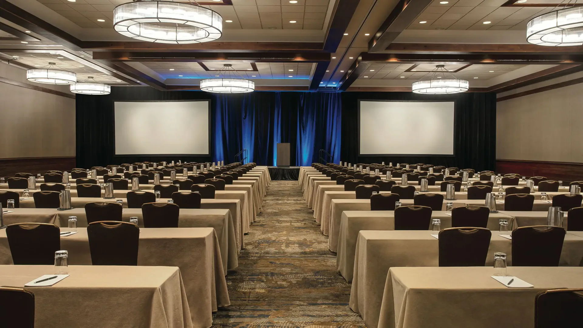Conference room setup with rows of tables and projection screens.