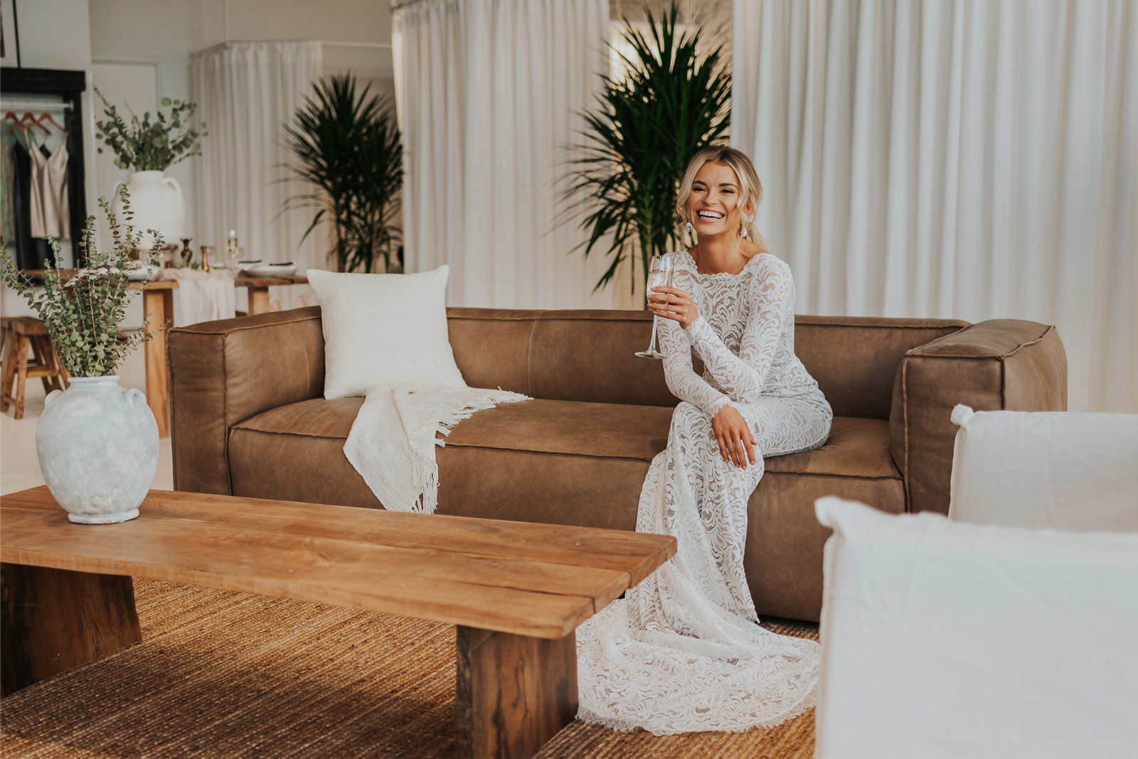 A woman in a white dress sitting on a couch in a bright room.