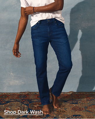 Person wearing dark wash jeans and a white t-shirt, standing barefoot.