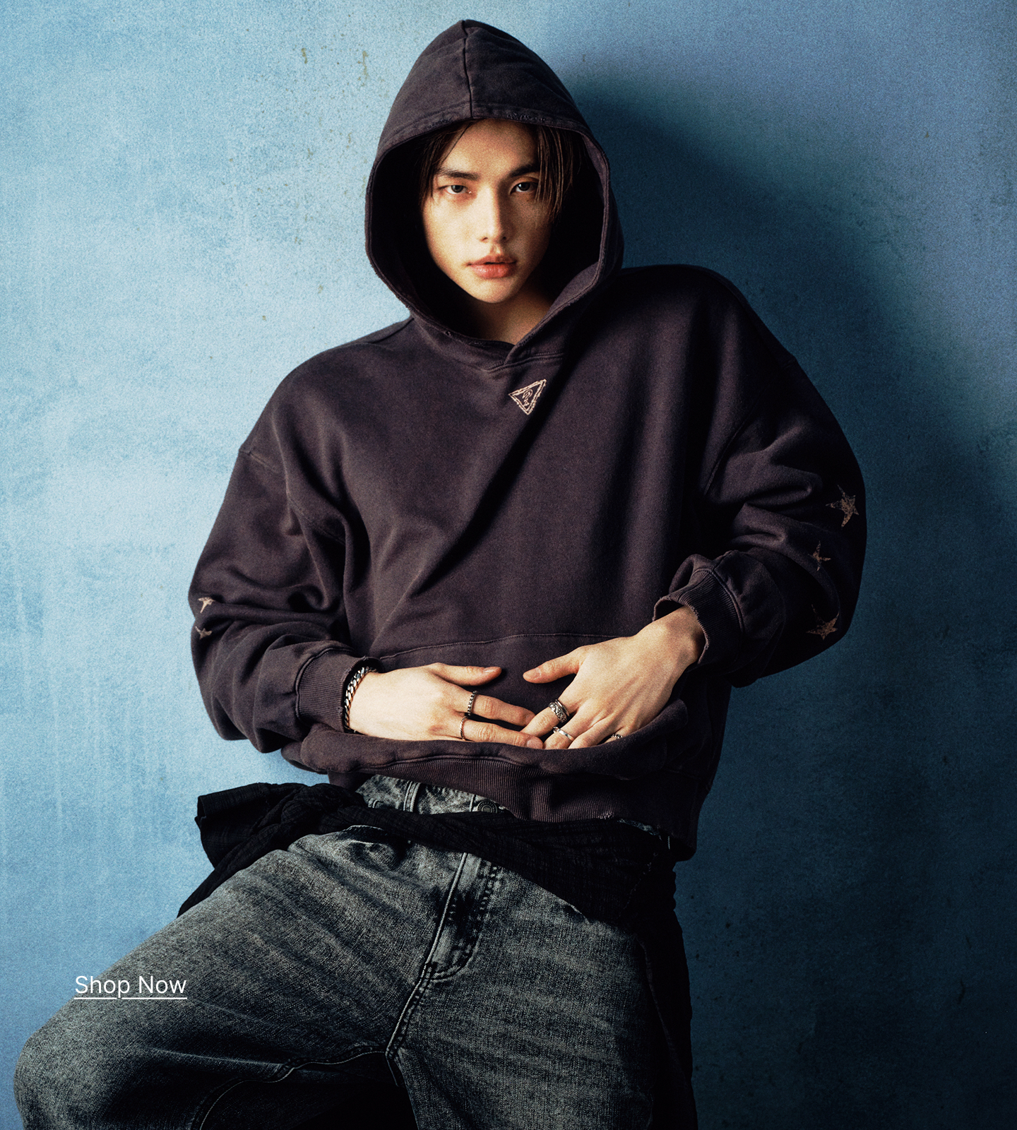 Hyunjin in a GUESS x Hyunjin hoodie posing against a blue wall.