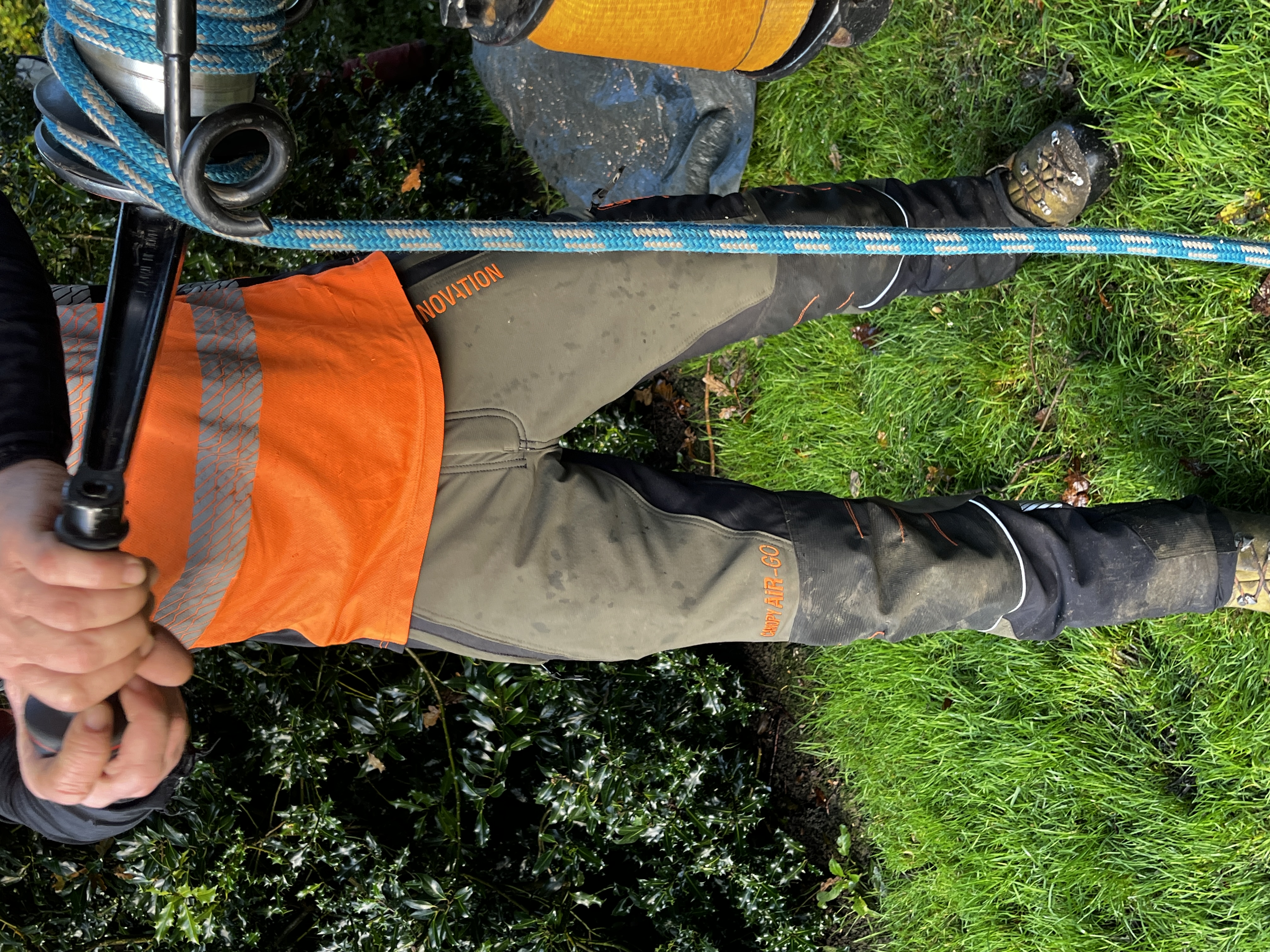 Person in workwear holding equipment with a blue rope on grass.