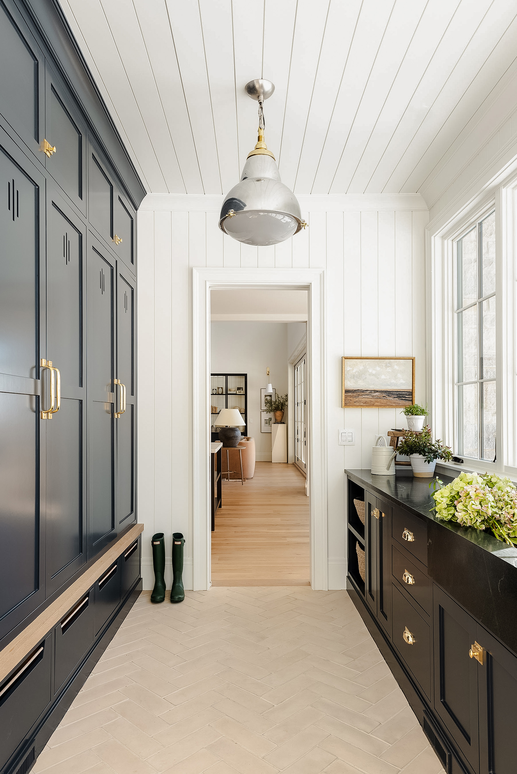 Timeless mudroom design by Studio McGee with dark navy cabinetry, brass hardware, white wooden panelling, and wood flooring