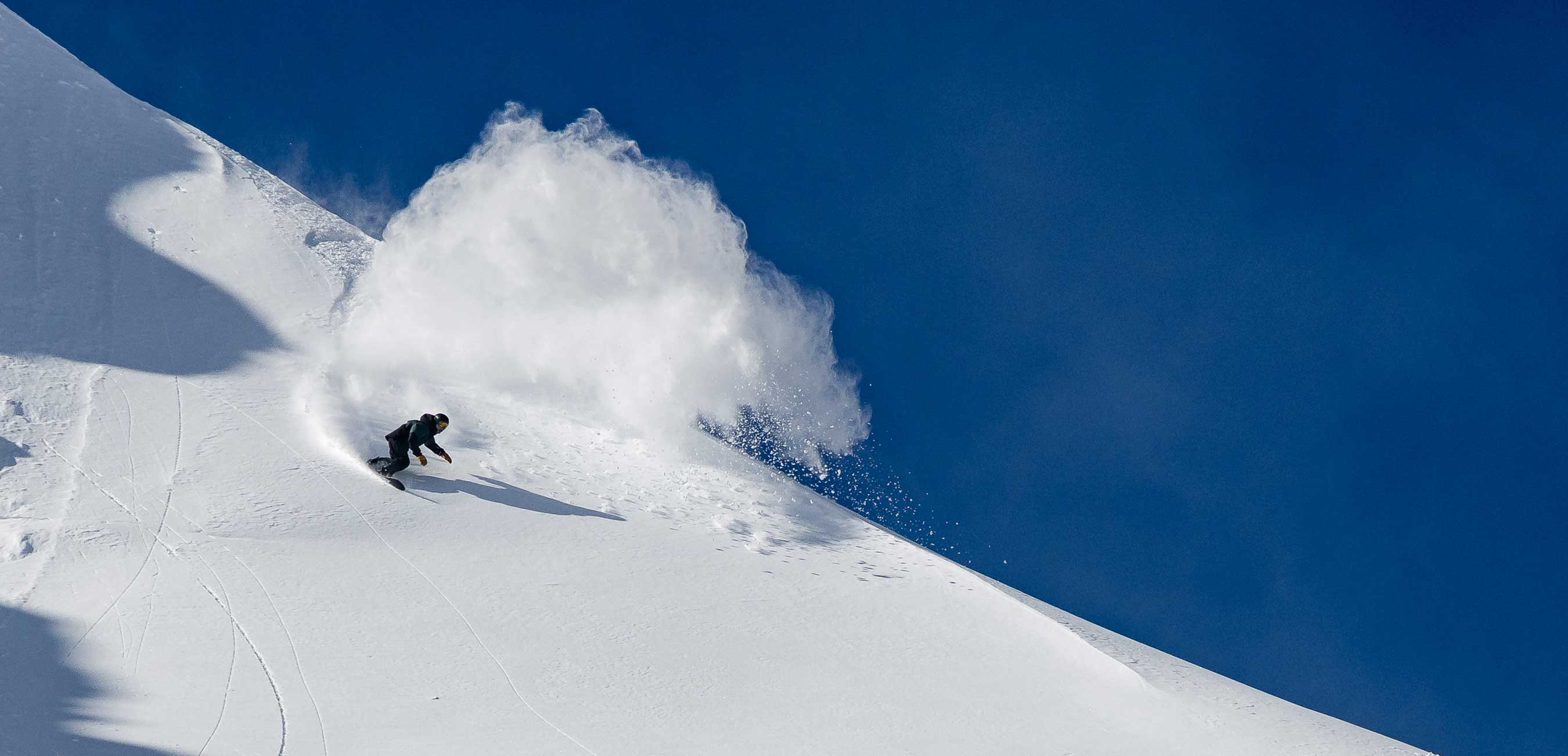 A snowboarder carving through fresh snow against a clear blue sky.