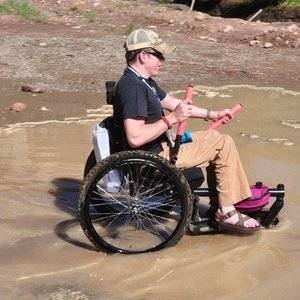 Adult uses GRIT Freedom Chair off road wheelchair through shallow water and mud