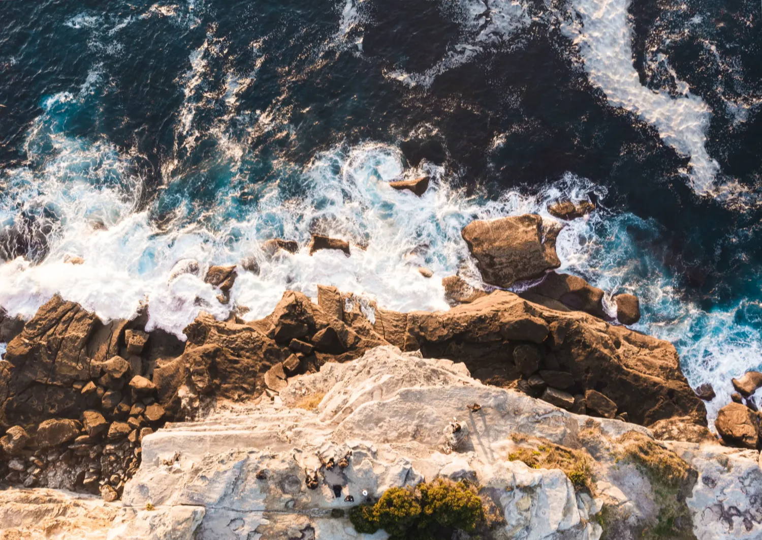 Overhead shot of a rocky cliff's edge looking  down into the ocean