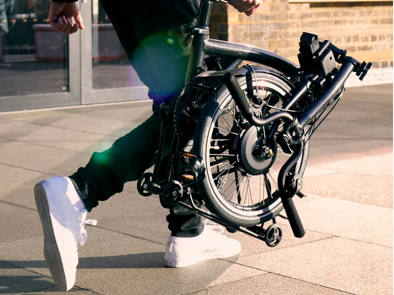 A man carries a folded Brompton Electric P Line bike