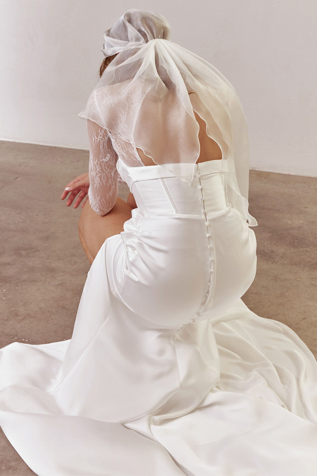 Bride in a wedding dress kneeling, wearing a veil and sheer headscarf.