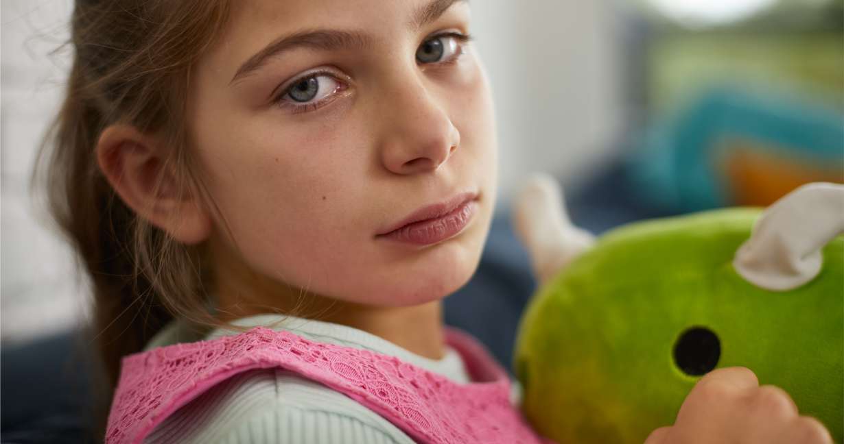 Child looking unwell and hugging her stuffed toy – she has dark circles under her eyes, an allergy symptom, and no fever