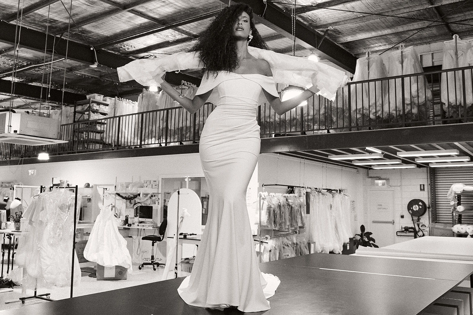 Model in a white dress walking on a runway in a bridal shop.