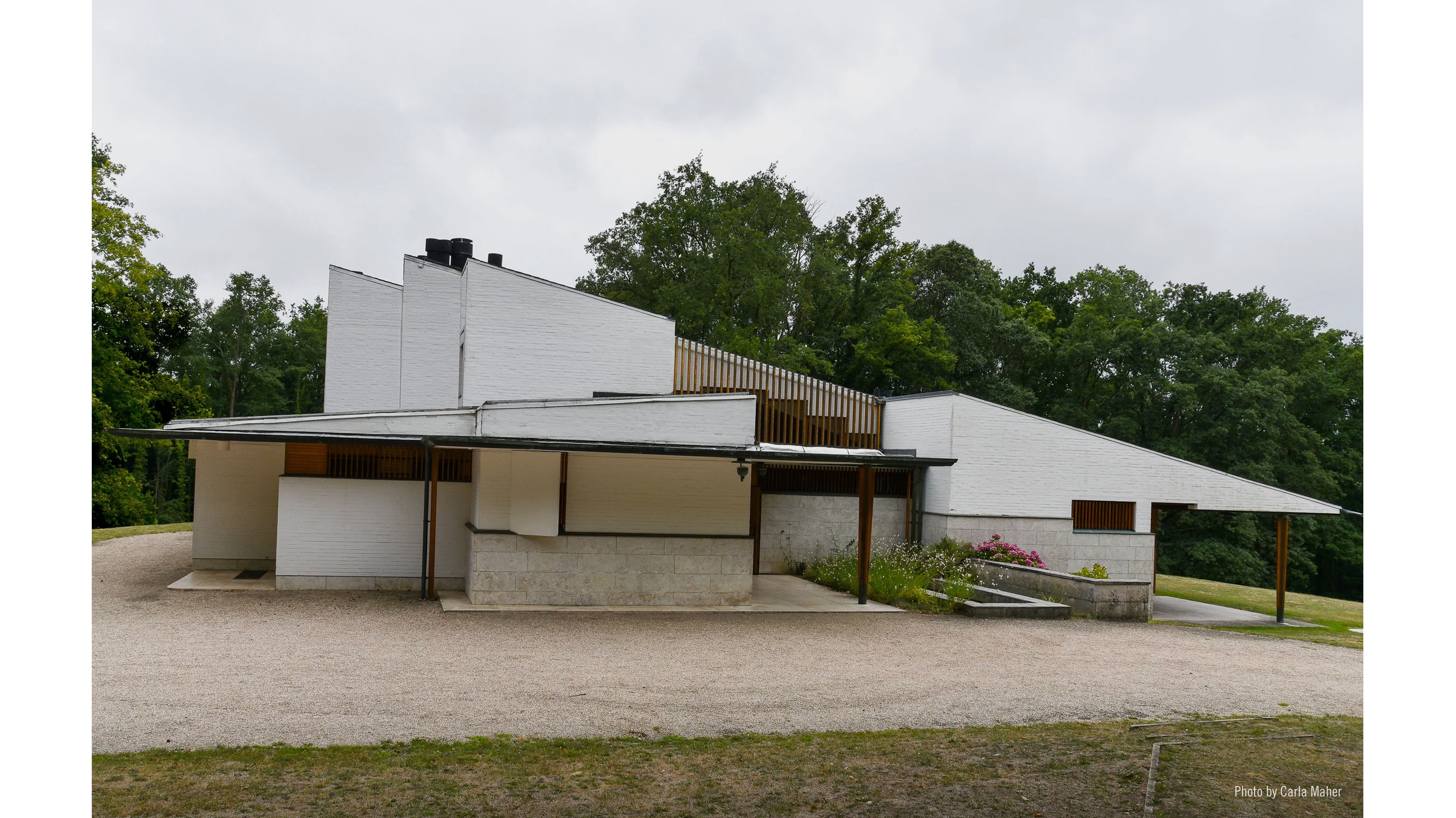 Modern architectural building surrounded by greenery under cloudy skies.