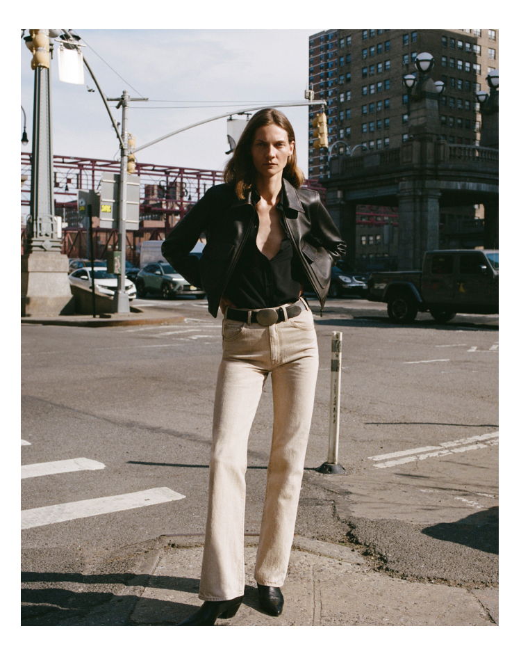 A person standing on a street, wearing a black shirt and beige pants.