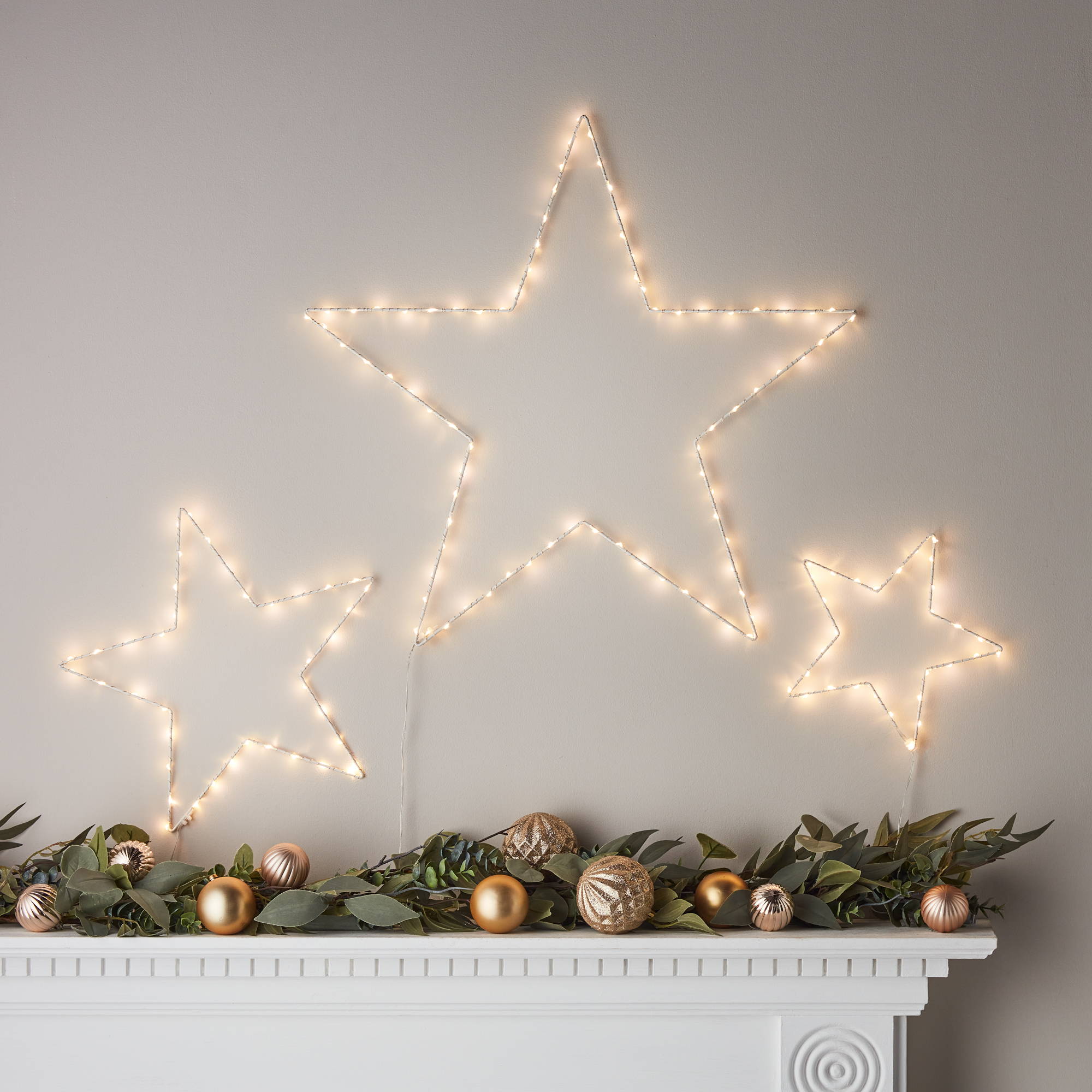 3 star lights above a mantlepiece with a Christmas garland.