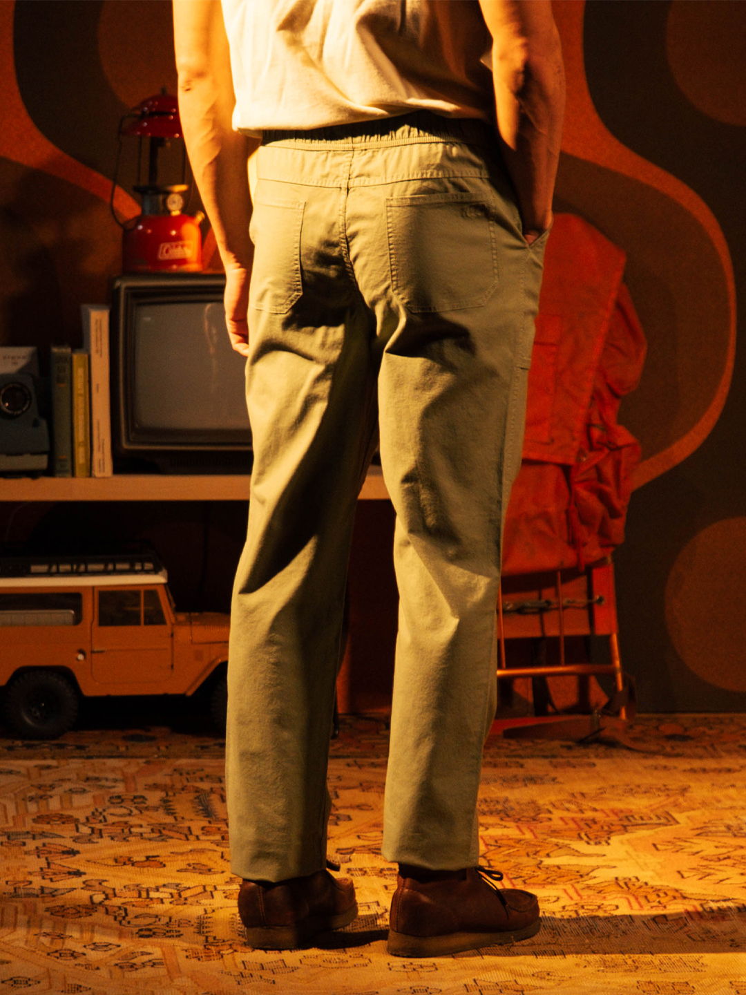 Person standing with hands in pockets, wearing light-colored pants in a retro setting.
