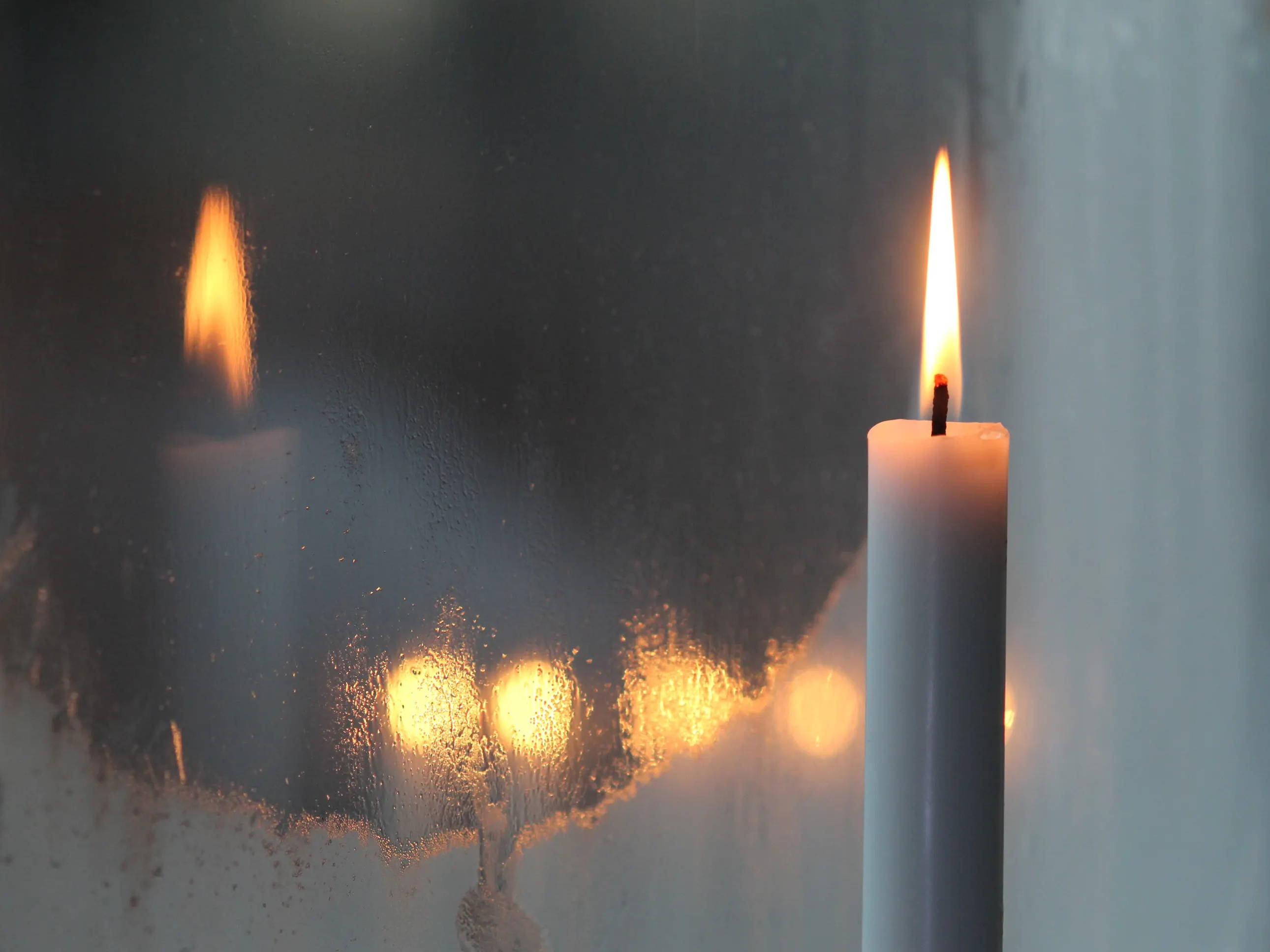 Lit taper candle burning in a frosty window