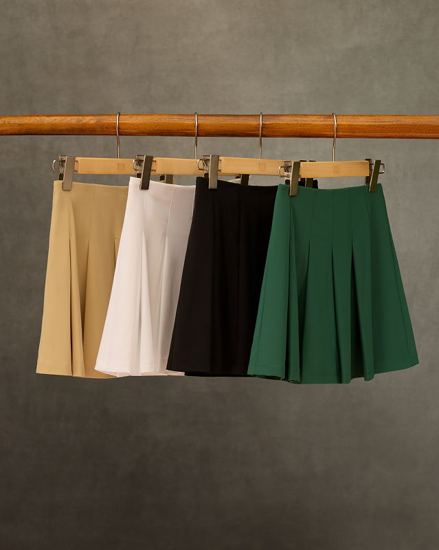 Four skirts in beige, white, black, and green hanging on a rack.