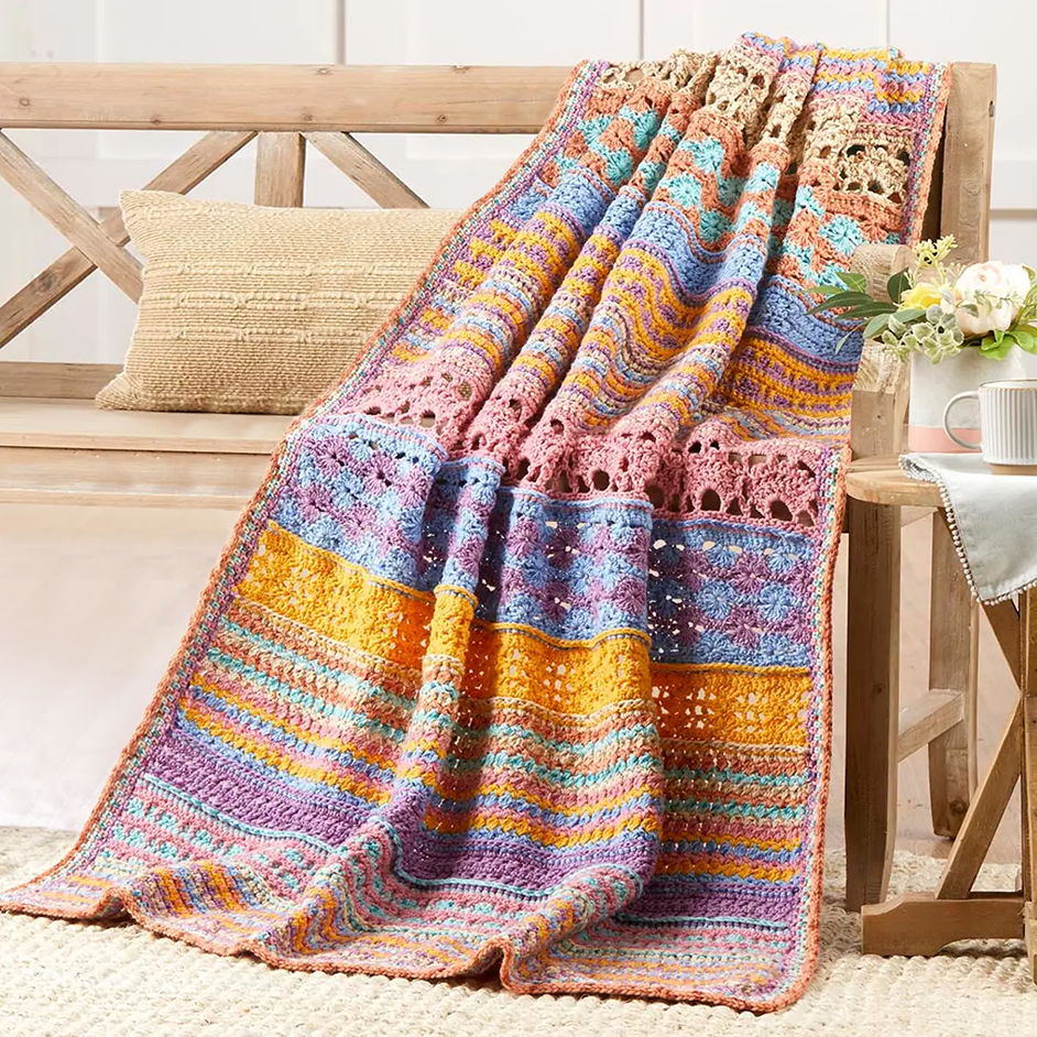 Colorful crochet blanket draped over a wooden bench with decorative pillows.
