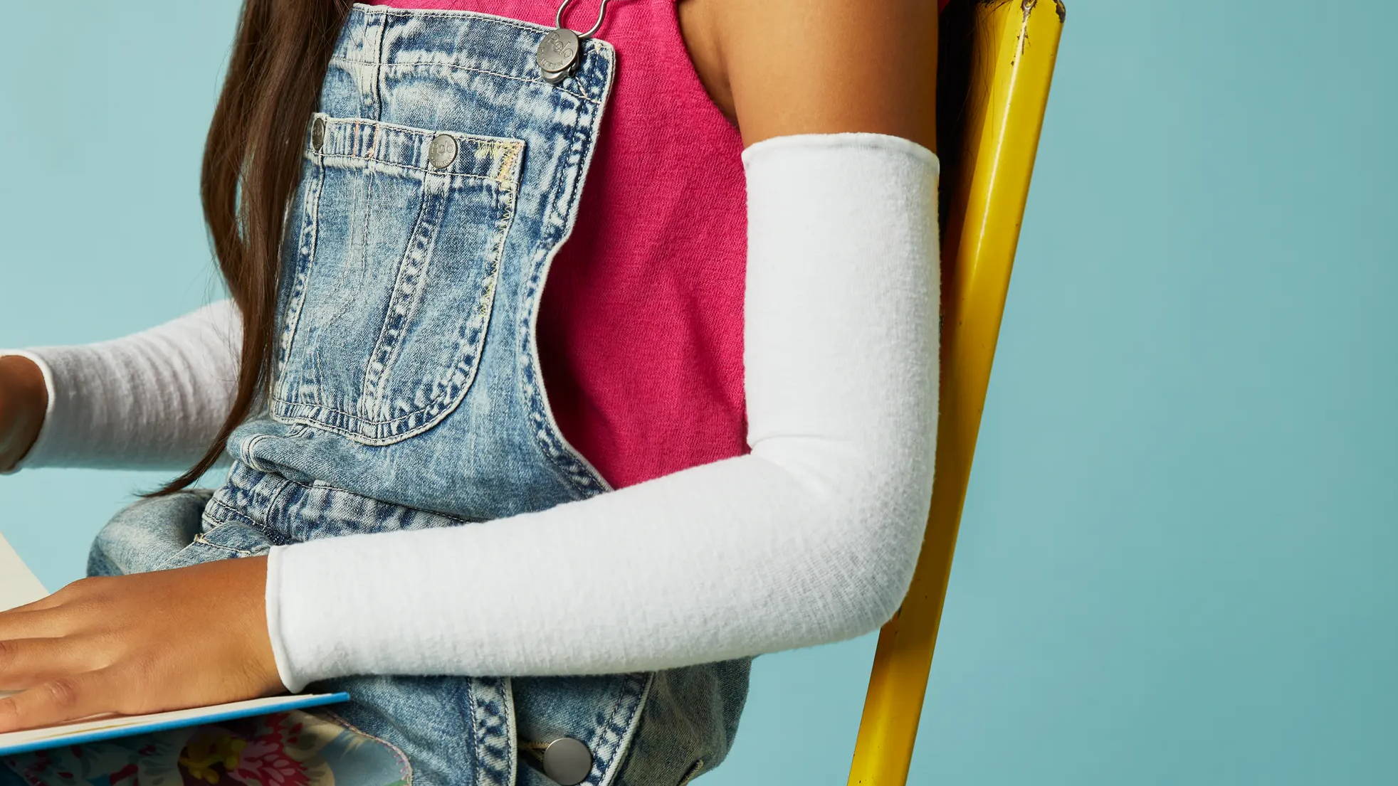 Girl focusing at desk, Girl in overalls wearing SmartKnitKIDs arm sleeves 