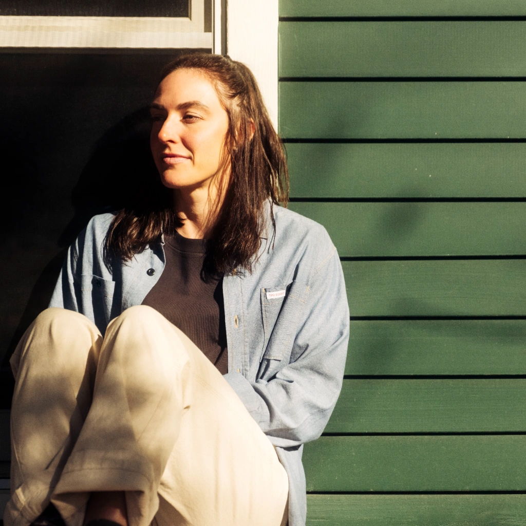 Person sitting by a green wall, looking contemplative in natural light.