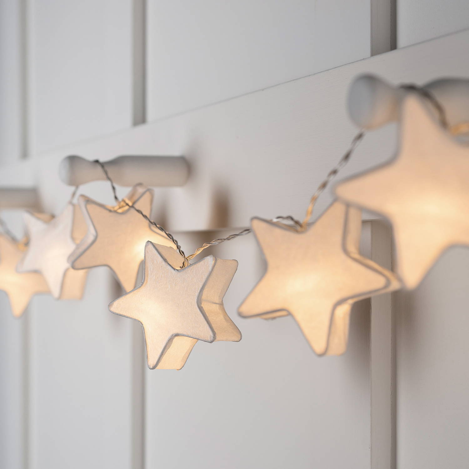 Warm white paper star lights hanging over pegs.