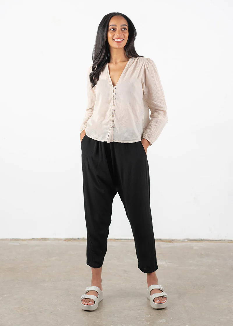 A model wearing an oatmeal coloured long sleeve button down shirt with black drop crotch cropped trousers and off white platform buckle slides