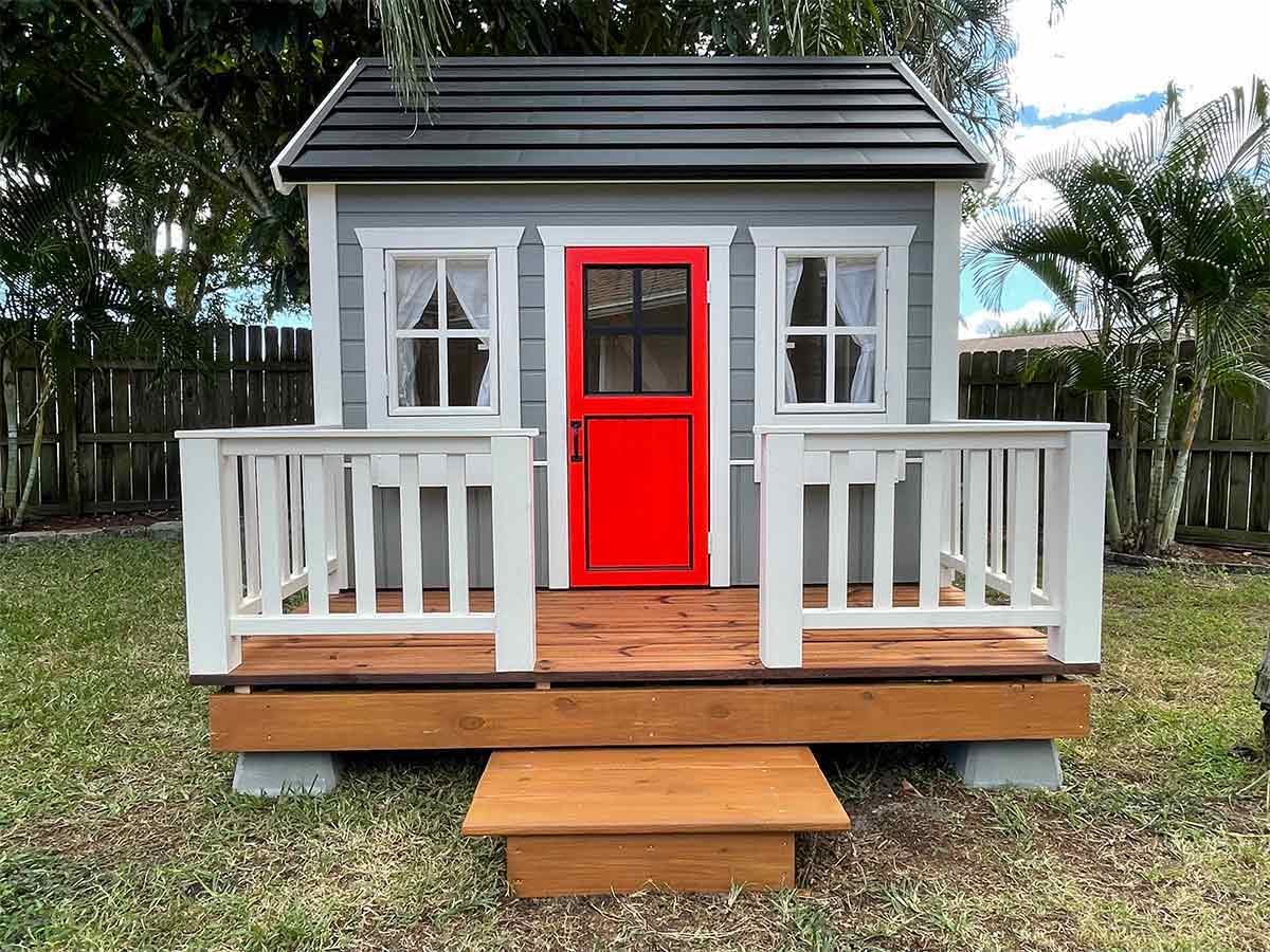 Custom Playhouse with bright red glass door in a backyard by WholeWoodPlayhouses