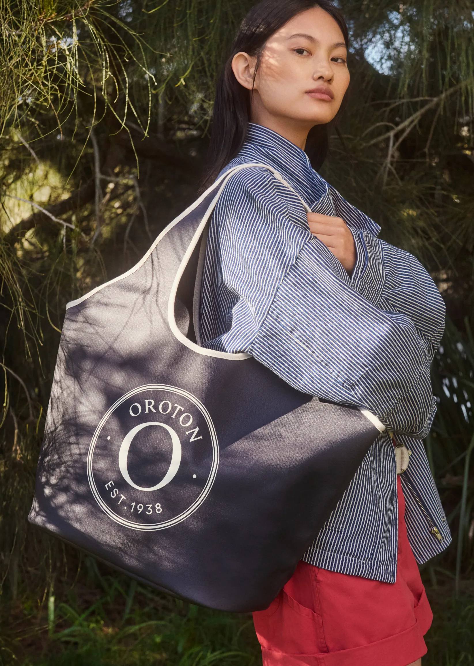 Model holding a large Oroton tote bag outdoors.
