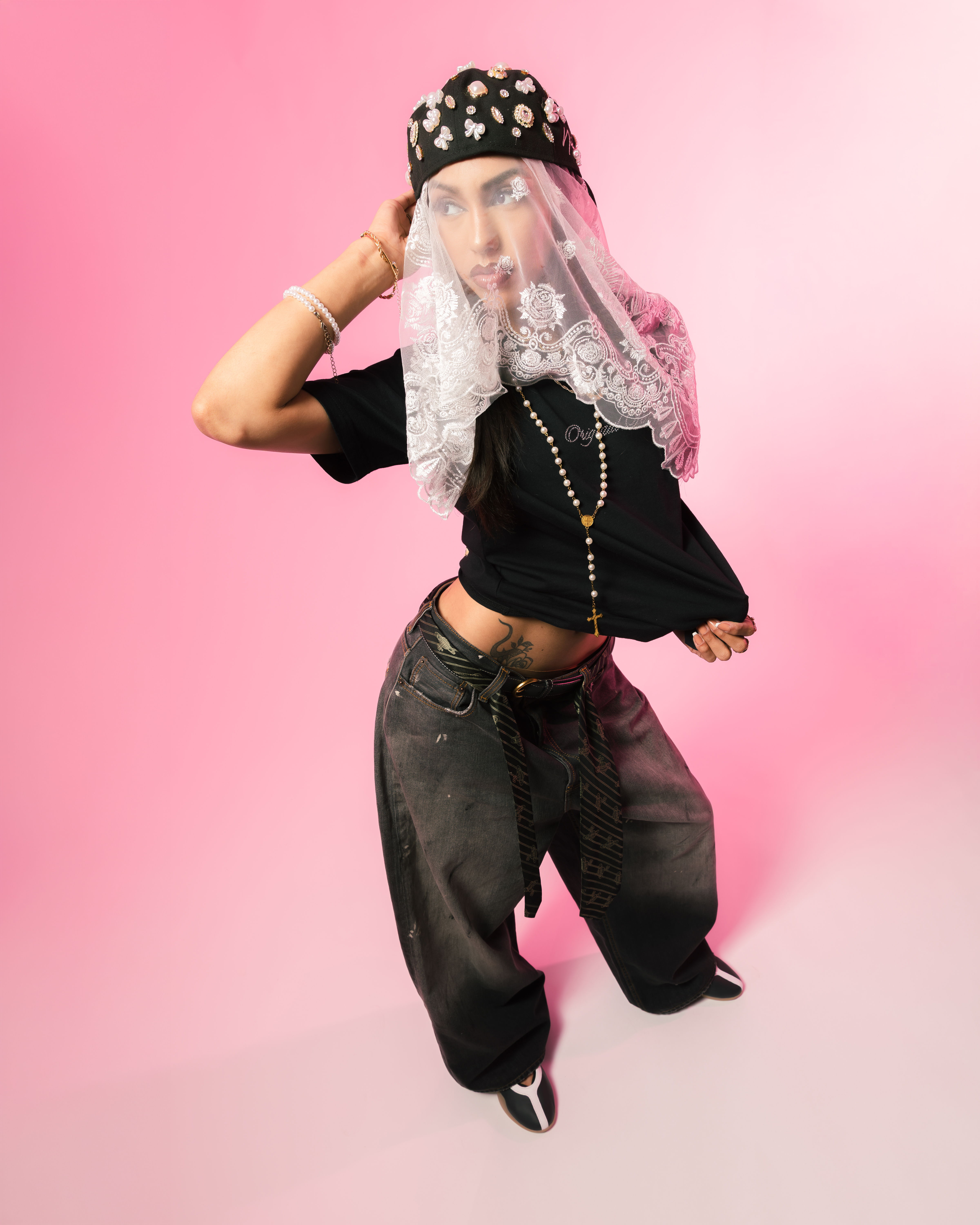 A person posing in stylish clothing against a pink background.