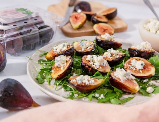 Plated figs with cheese on arugula, surrounded by fresh figs and blueberries.