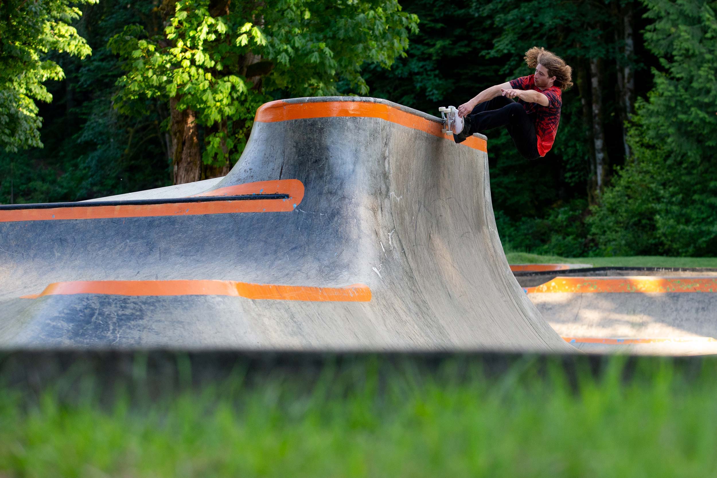 Skateboarder performing tricks on a concrete skate park ramp surrounded by greenery.