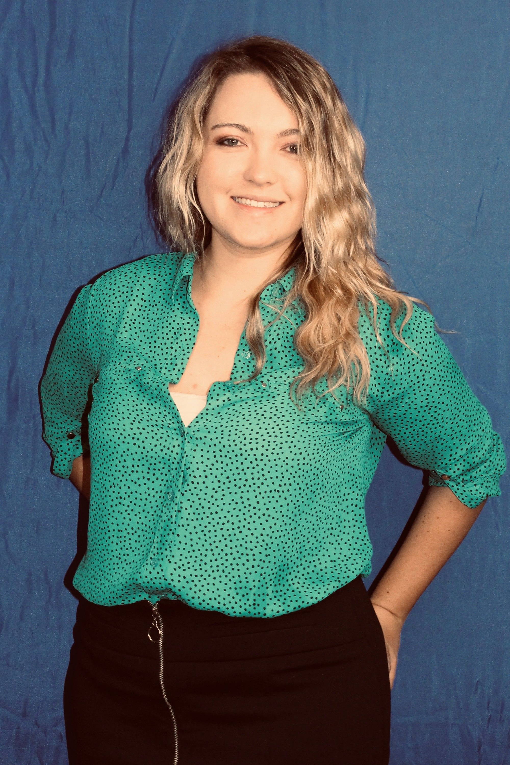 Smiling woman with wavy hair, wearing a green blouse against a blue background.