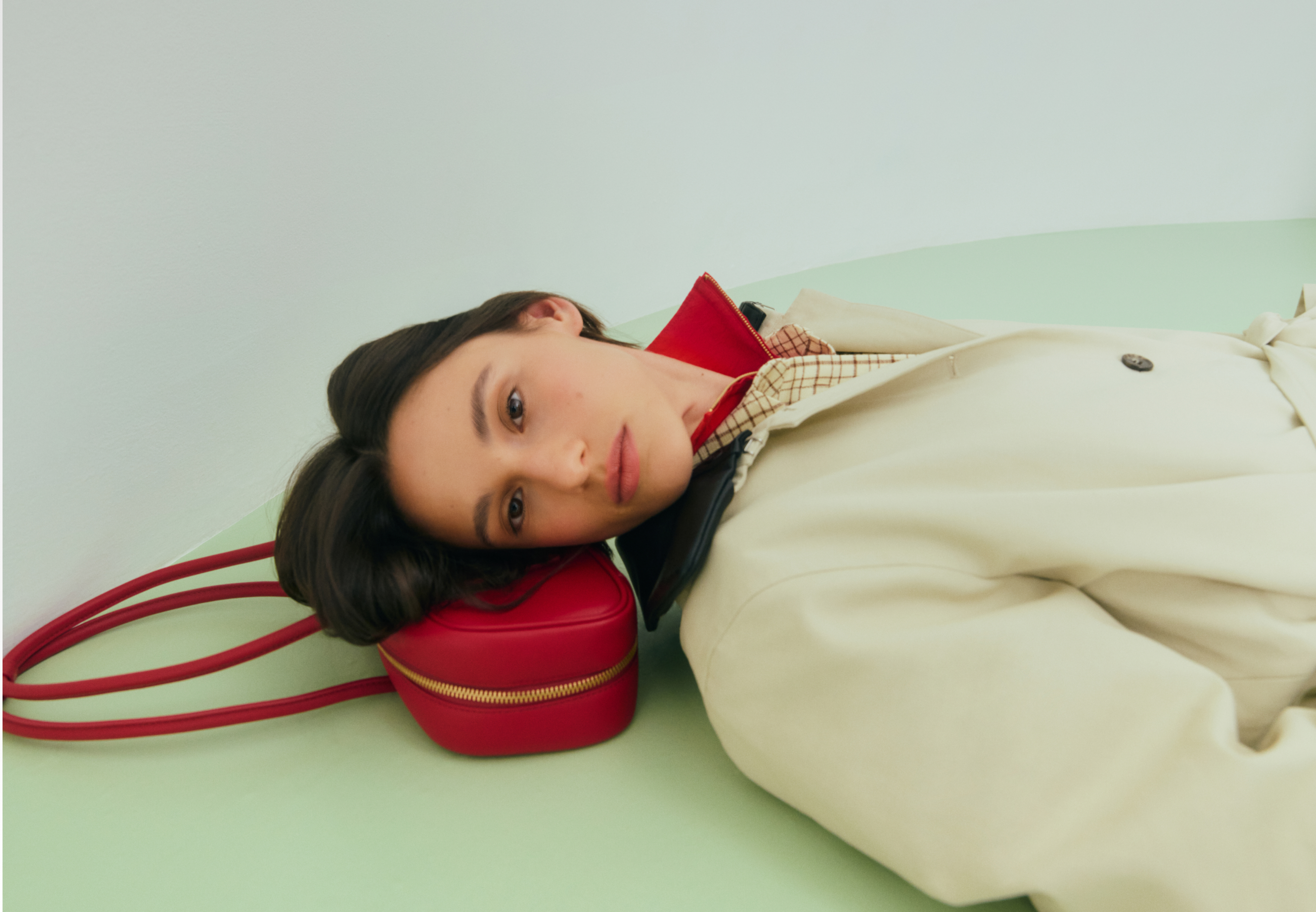 Person leaning on a green surface with a red handbag beside them.