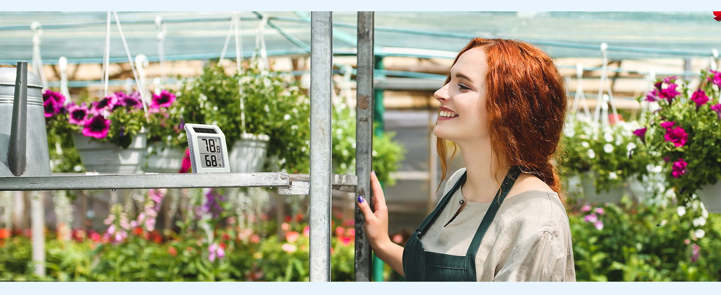 A woman in an apron smiles among colorful flowers in a greenhouse.
