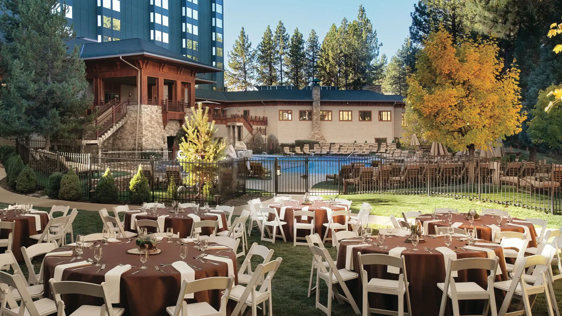 Outdoor event space with tables, surrounded by trees and a pool.