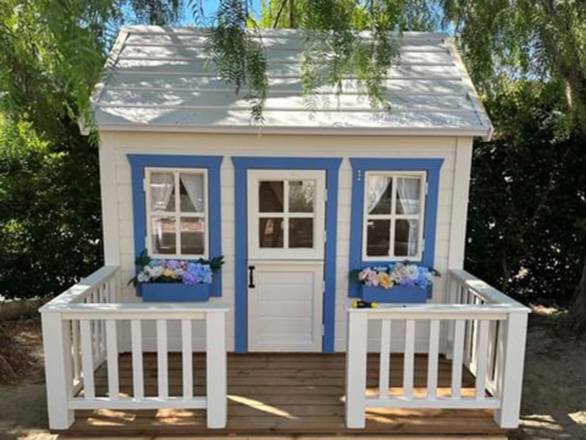 White and Blue Outdoor Playhouse Natural Wonder with blue Flower boxes and wooden terrace with railings in a backyard by WholeWoodPlayhouses